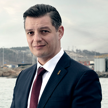 Elvir Dzanic in a suit looking at the camera, in front of a harbour.