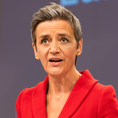 Margrethe Vestager speaking in a red blazer in front of a grey background.