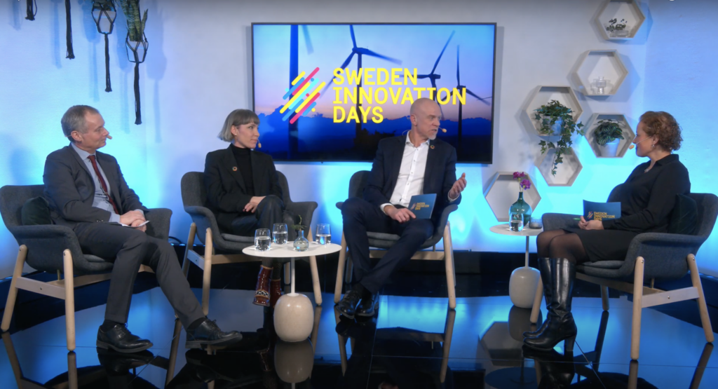 Impact Innovation Fireside chat with the three director generals sitting in chairs opposite Regina Summer who is moderating the chat. all are sitting in a blue lit room with a screen behind them with the Sweden Innovation Days logo